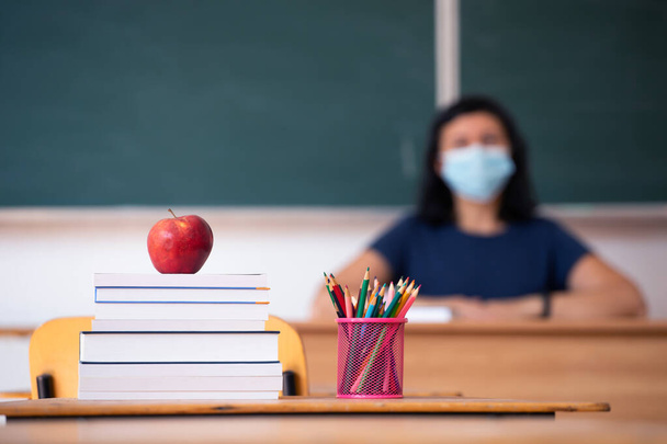 Back to School Concept. Apple, accessories and books in the classroom, teacher wearing mask in the background. - Photo, Image