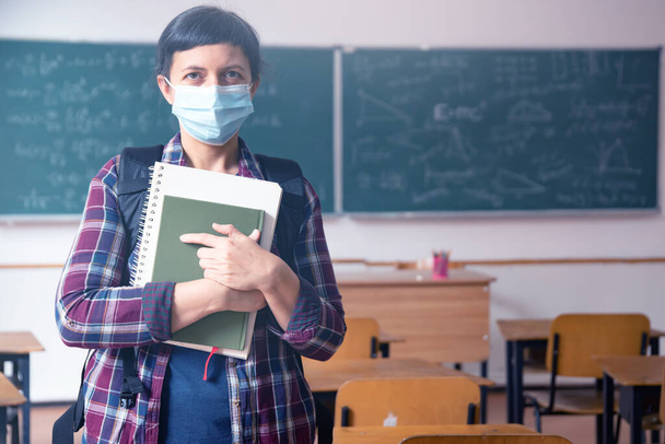 Smiling student girl wearing school backpack, mask and holding exercise book. Social distanting and classroom safety during coronavirus epidemic - Φωτογραφία, εικόνα