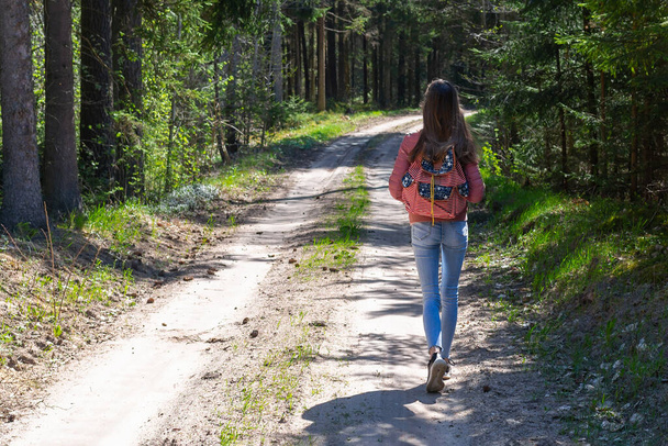 Uma jovem turista com mochila caminhando ao longo do caminho pela floresta durante o dia de verão. Estilo de vida Hipster e viagem a solo.Visão traseira. - Foto, Imagem