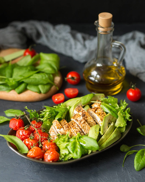 Итальянская кухня. Зеленый здоровый салат на темном фоне. Зеленая органическая еда. Салат из запеченной курицы и помидоров. Салат с авокадо, шпинат и базилик. Стиль салатной еды. Оливковое масло - Фото, изображение