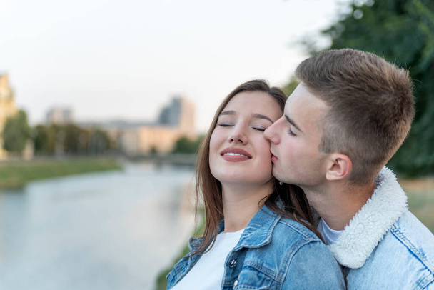 川の上の若い愛情のカップルの肖像画。男は頬に最愛のキス。ロマンチックなデート. - 写真・画像