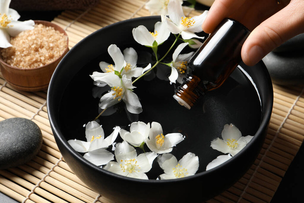 Woman dripping jasmine essential oil into bowl on table, closeup - Foto, Imagem