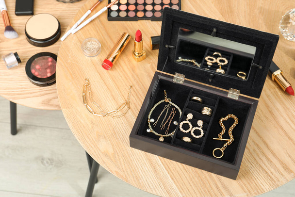 Jewelry box with stylish golden bijouterie and makeup products on wooden table, above view - Photo, image