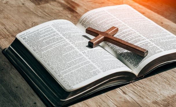 Крест поверх открытой библии на деревянном столе с окном light.christian backgound - Фото, изображение