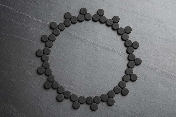Frame of activated charcoal pills on black table, flat lay with space for text. Potent sorbent - Фото, изображение