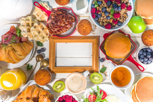 Various traditional breakfast food - fried eggs with bacon, muesli, oats, waffles, pancakes, burger, croissants, fruit berry, coffee, tea and orange juice, white table background copy space top view - Foto, Bild
