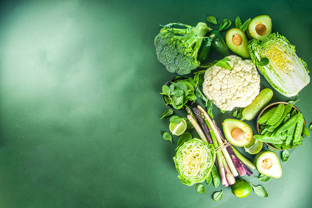 Gezonde voeding Voorjaar voedsel achtergrond. Assortiment van verse rauwe biologische groene groenten - broccoli, bloemkool, courgette, komkommers, asperges, spinazie, avocado, kool op donkergroene achtergrond - Foto, afbeelding