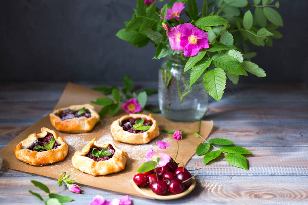 Baked small biscuits with cherries on a wooden table. Summer cakes with berries and pink flowers in the rustic style - 写真・画像
