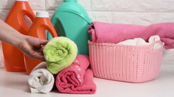 een plastic mand met gewassen droge opgerolde handdoeken en een oranje fles met vloeibaar wasmiddel tegen een achtergrond van een witte bakstenen wand - Video