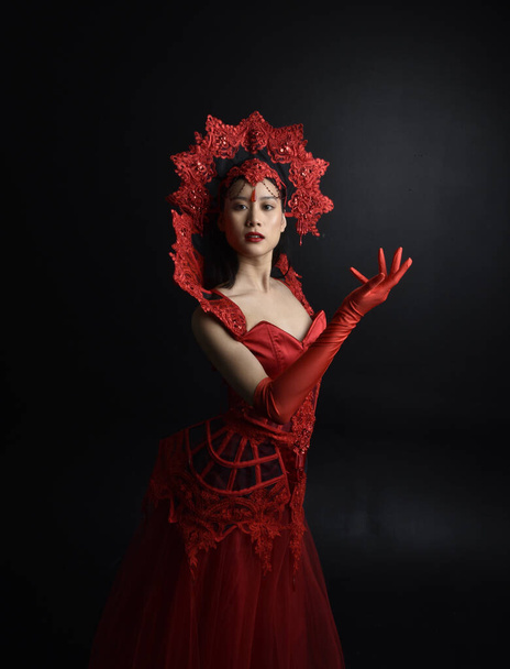 Portrait complet de belle jeune femme asiatique portant un corset rouge, de longs gants d'opéra et une couronne de reine gothique ornée. Pose gracieuse isolée sur un fond de studio sombre. - Photo, image