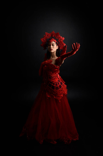 drámai portré gyönyörű fiatal ázsiai nő visel piros fűző, hosszú opera kesztyű és díszes gótikus királynő koronát. Kecses pózolás elszigetelt sötét stúdió háttér. - Fotó, kép