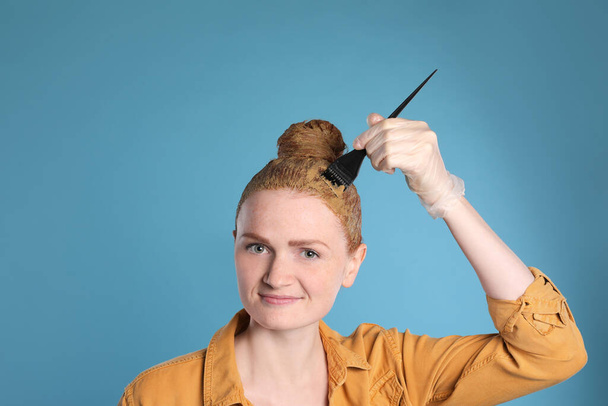 Young woman dyeing her hair with henna on light blue background - Photo, image