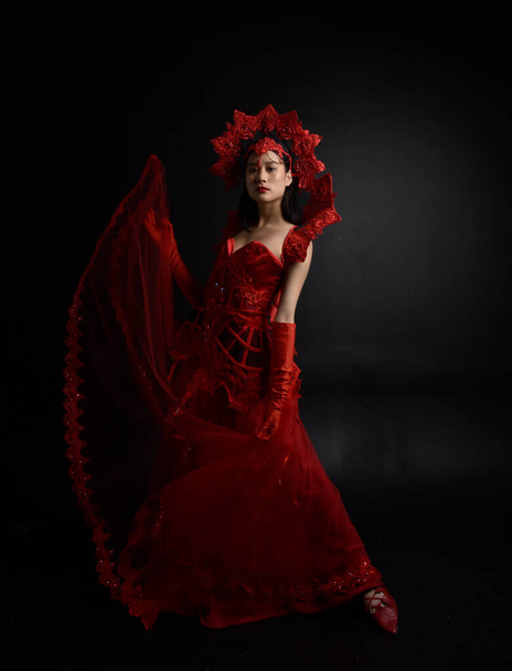 赤のコルセット、長いオペラ手袋、華やかなゴシック女王の王冠を身に着けている美しい若いアジアの女性の劇的な肖像画。暗いスタジオの背景に隔離された優雅なポーズ. - 写真・画像