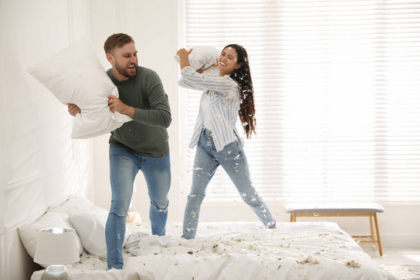 Happy young couple having fun pillow fight in bedroom - Fotoğraf, Görsel