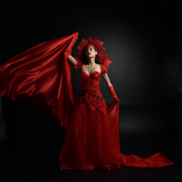 赤のコルセット、長いオペラ手袋、華やかなゴシック女王の王冠を身に着けている美しい若いアジアの女性の劇的な肖像画。暗いスタジオの背景に隔離された優雅なポーズ. - 写真・画像