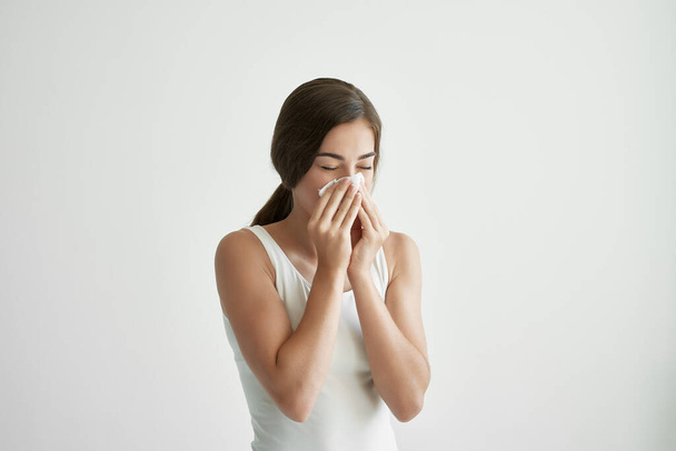 Frau im weißen T-Shirt pustet sich die Nase in ein Taschentuch - Foto, Bild