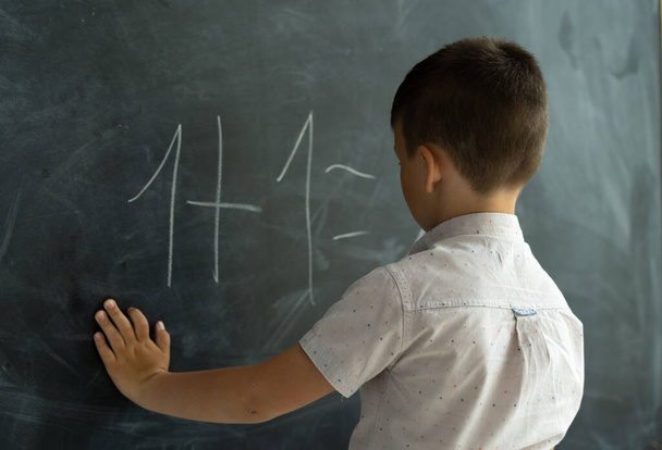 schoolboy in the class near the blackboard writes numbers with chalk. Math lesson. Junior School. The concept of modern education. Back to school. Place for text. - Foto, afbeelding
