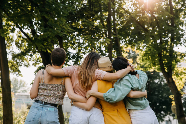Group of four women in a park, hugging together from behind. - Foto, imagen