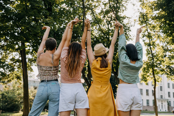 Group of four women outdoors, having good time, holding hands up in the air. - Foto, afbeelding