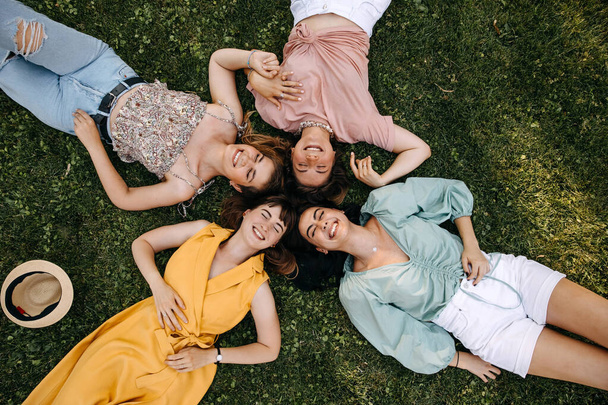 Négy fiatal nőből álló csoport, akik zöld füvön fekszenek a szabadban, egy parkban, jól érzik magukat.. - Fotó, kép