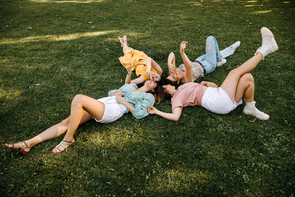 Четыре молодые женщины, лежащие на зеленой траве, на открытом воздухе, в парке, смеясь. - Фото, изображение