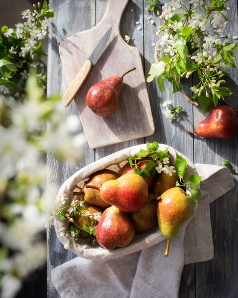 Een verse oogst peren. Bloeiende planten en voedsel op een houten tafel. Gele vruchten in een rustieke stijl. In het proces van het maken van een peer taart - Foto, afbeelding