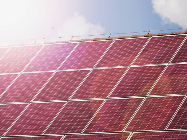 Červené solární panely na střeše domu, koncept obnovitelné energie. Horký odraz slunce ve fotovoltaickém krytu fólie - Fotografie, Obrázek