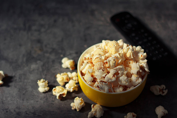 Close-up top view picture white popcorn in a yellow bowl with remote control for watch TV. Made of corn is a delicious food or snack to eat in the cinema use it as a background image. - Foto, Imagen