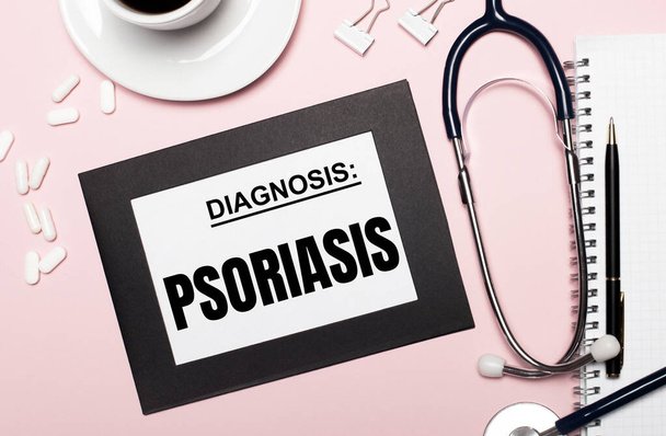 On a light pink background, a notebook with a pen, stethoscope, white pills, paper clips and a sheet of paper with the text PSORIASIS. Medical concept - 写真・画像