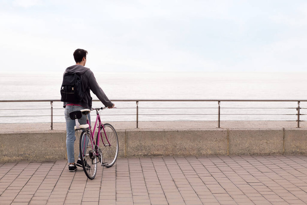 vista trasera de un joven caminando con una bicicleta, concepto de transporte sostenible y estilo de vida urbano, espacio para copiar texto - Foto, Imagen