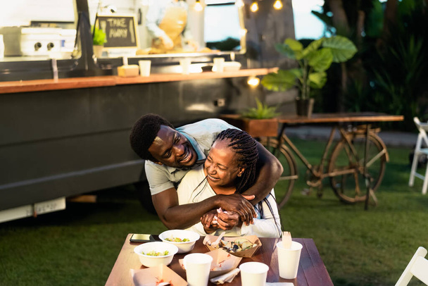 Happy Afro mother and son having fun eating in a street food truck market outdoor - Foto, Imagem