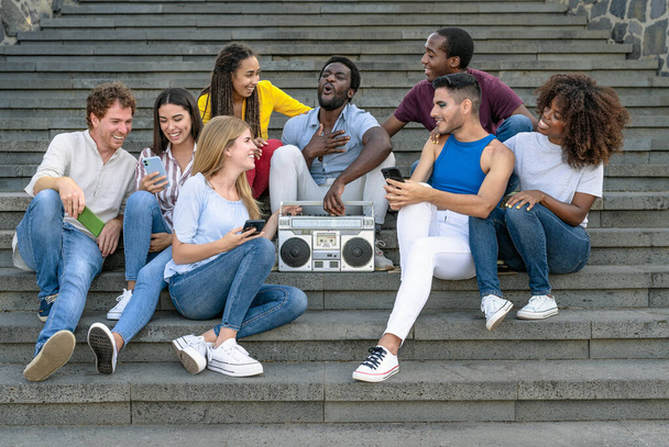 Genç çok ırklı arkadaşlar, klasik teyp teybiyle müzik dinlerken ve şehir merdivenlerinde otururken cep telefonu kullanırken eğleniyorlar - Gençlik milenyum yaşam tarzı konsepti - Fotoğraf, Görsel