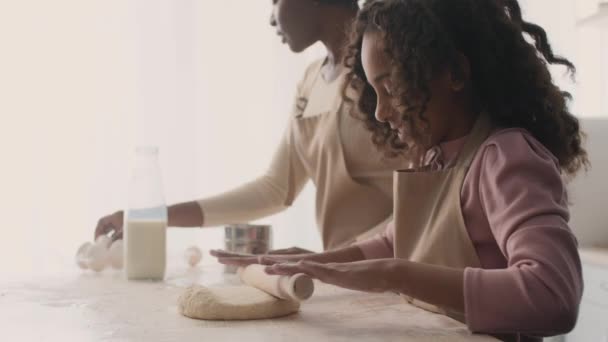 Aranyos kis afro-amerikai lány roll ki nyers tészta fa pin, előkészítése házi pite anyával a konyhában - Felvétel, videó