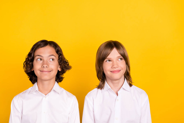 Photo of two dreamy inspired schoolboys look empty space wear white shirt isolated yellow color background - Фото, изображение