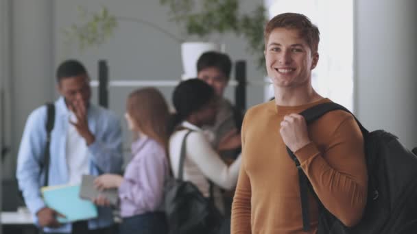 Впевнений хлопець з рюкзаком посміхається до камери, позує в коледжі через спілкування з різними однокласниками на фоні
 - Кадри, відео