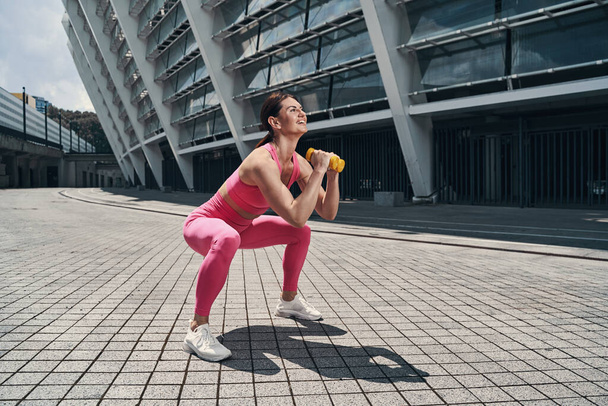 Joyful sportive woman squatting with hand weights - Фото, зображення