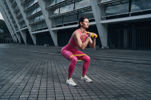 Sportswoman doing squats with resistance band on legs - 写真・画像