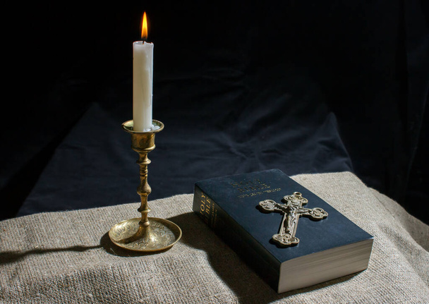 brązowy krzyż, płonąca świeca i Biblia na stole zamknięcie wnętrz - Zdjęcie, obraz
