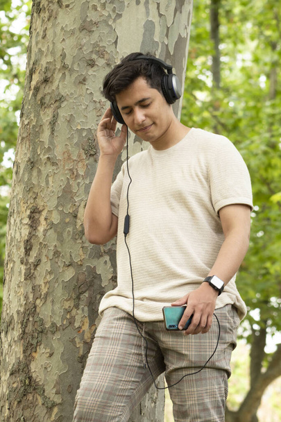 Morena hispana niño escuchando música con auriculares y ropa amarilla en un bosque verde sonriendo - Foto, Imagen