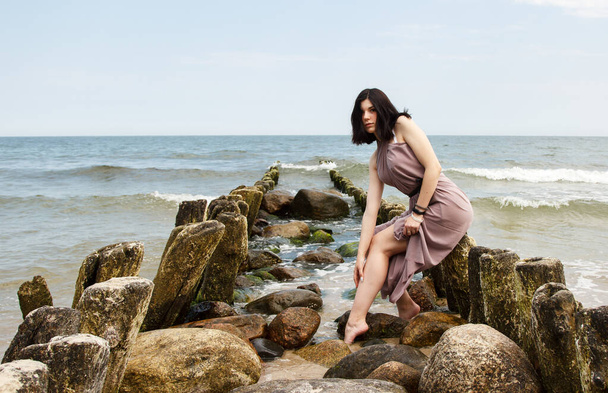 fiatal barna nő bézs ruha ül egy törés a tenger mellett a nyári napon - Fotó, kép