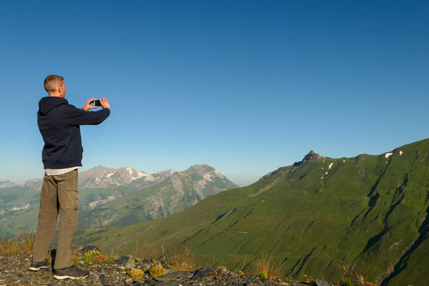 A man taking a picture with a smartphone in nature. Back hiker, at the top of a cliff, facing a mountain range - Foto, afbeelding