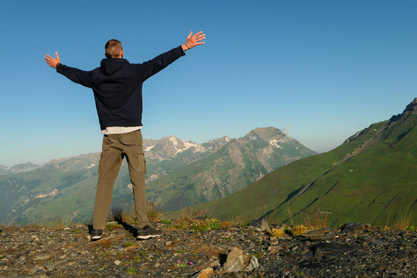 Mies takaapäin, vuorelle päin kesällä. Vaeltaja seisoo kädet ylhäällä taivasta kohti. Lumihuippuiset vuorenhuiput taustalla. Menestyksen käsite. - Valokuva, kuva