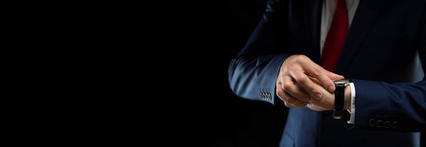Businessman looks at his watch on a black background with place for text - Foto, Imagen