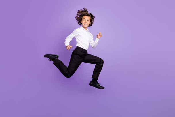 Full size photo of crazy small brunet boy jump wear shirt trousers sneakers isolated on purple color background - Фото, зображення