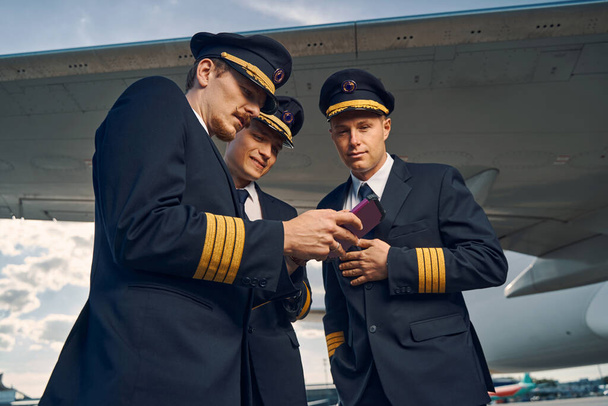 Três aviadores visualizando fotografias no smartphone - Foto, Imagem