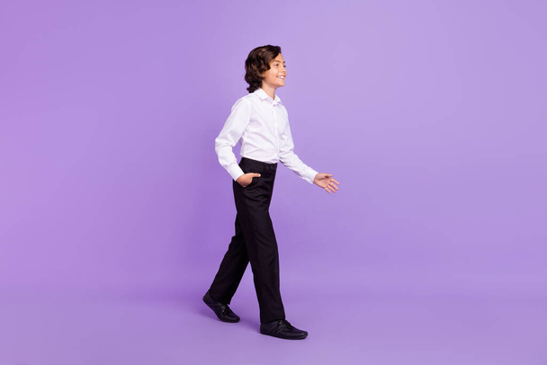 Full body profile photo of cute small brunet boy go wear formalwear trousers sneakers isolated on purple color background - Фото, изображение