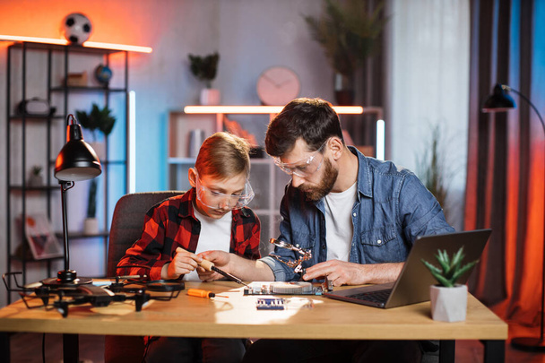 Boy with father soldering together details from laptop - Fotó, kép