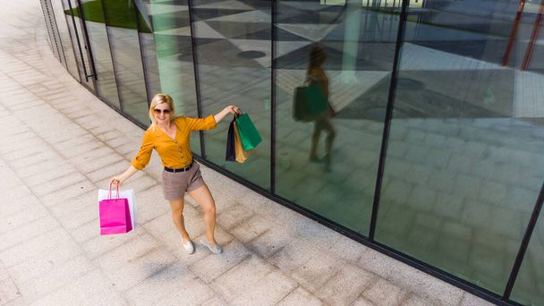 Glück, Konsum, Verkauf und Menschen-Konzept - lächelnde junge Frau mit Einkaufstüten vor Mall-Hintergrund - Foto, Bild