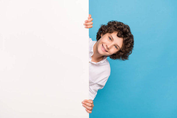 Photo of charming sweet schoolboy wear white shirt smiling holding arms placard empty space isolated blue color background - Foto, immagini
