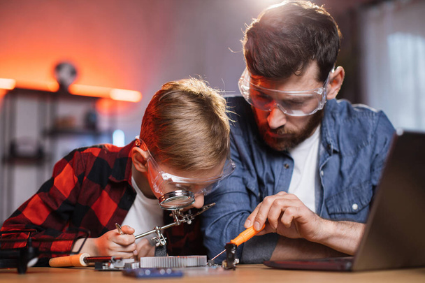 Boy soldering display card while father helping near - Фото, изображение